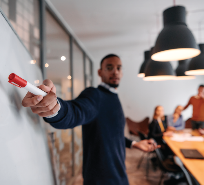 Business man points to a white board while holding a marker