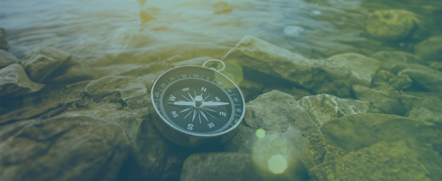 black and metal compass laying on rocks next to a water source at sunset