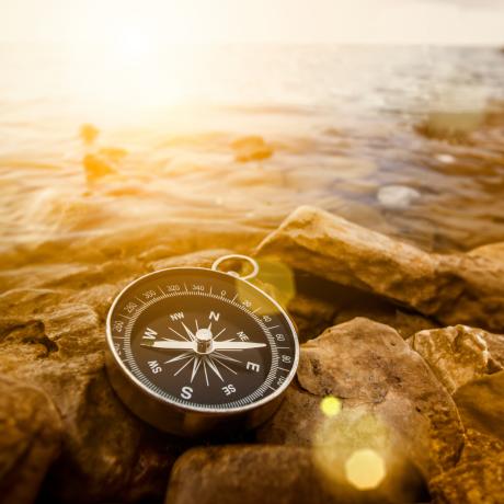 black and metal compass laying on rocks next to a water source at sunset