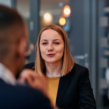 A woman wearing a yellow shirt is speaking to another unseen person