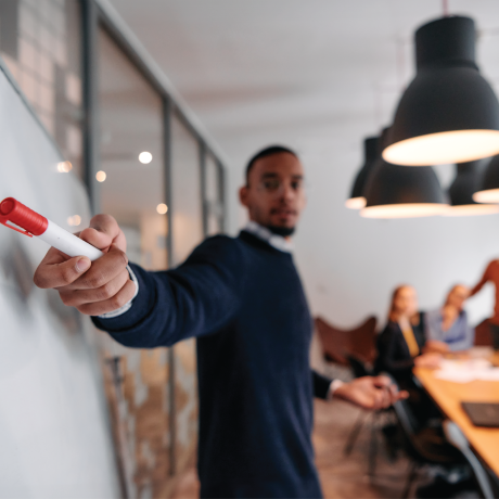 Business man points to a white board while holding a marker